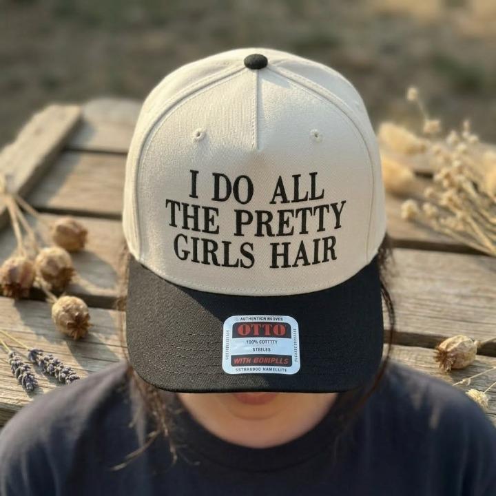 Person wearing a cream and black Pretty Girls Hair trucker cap