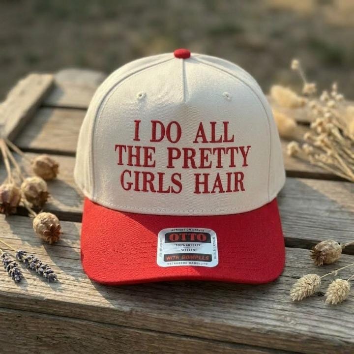 Cream and red Pretty Girls Hair trucker cap displayed on a wooden table