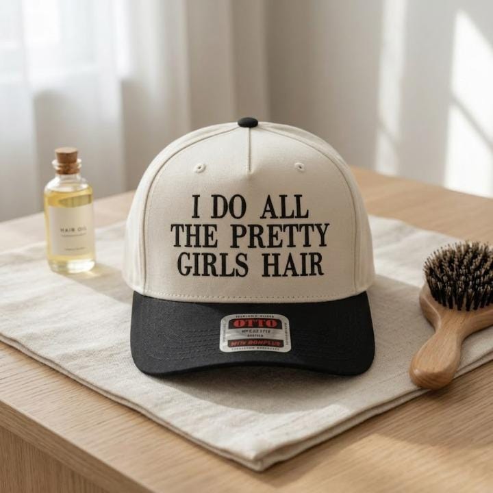 Pretty Girls Hair slogan hat styled beside a hairbrush and beauty accessories
