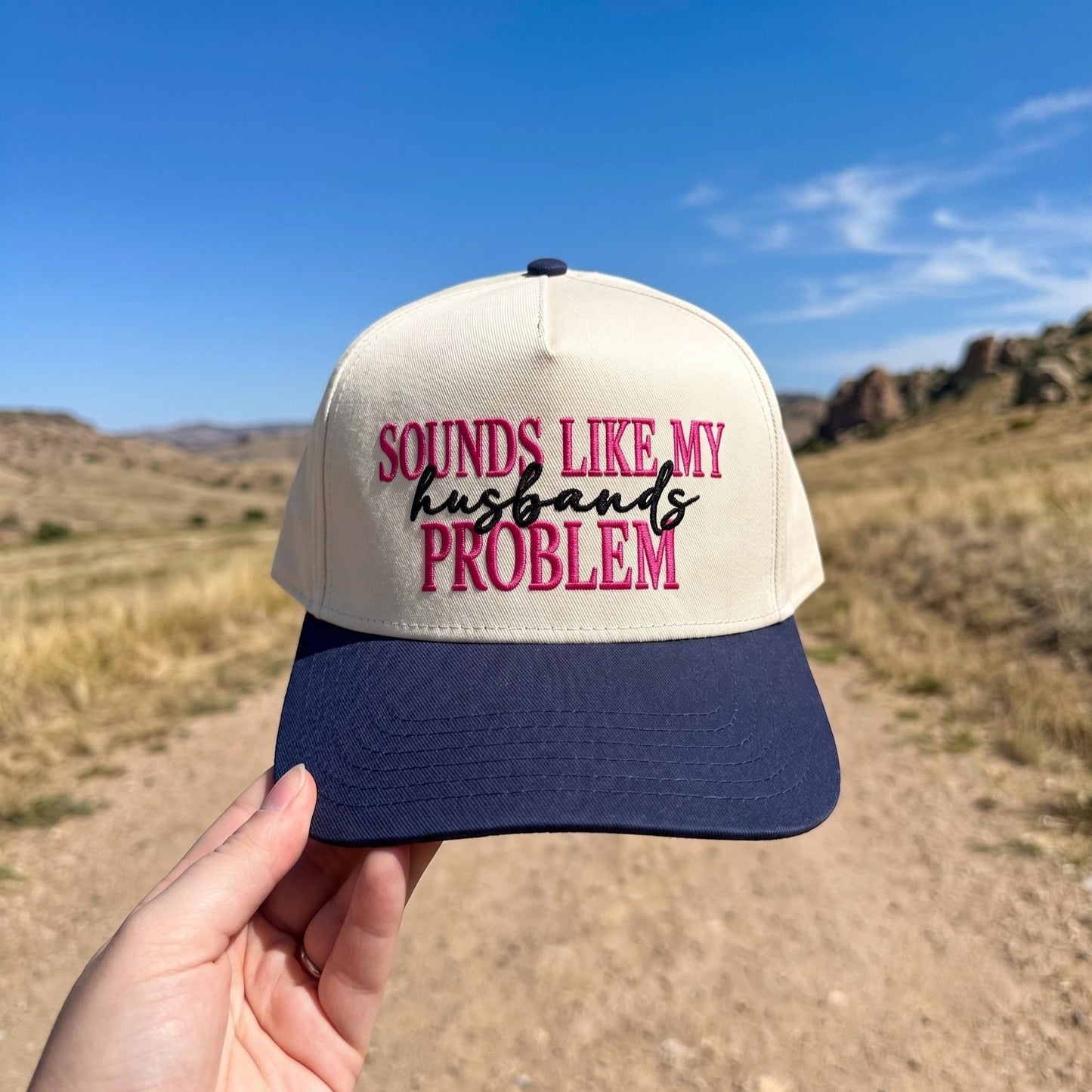 Embroidered trucker hat with cream front and navy brim featuring a sassy phrase in a desert setting