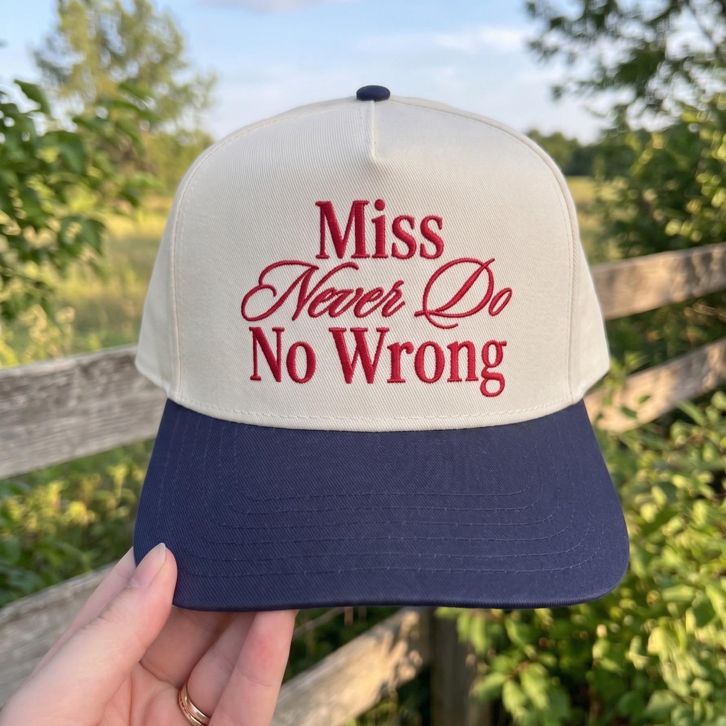 Trendy two-tone cap with 'Miss Never Do No Wrong' embroidery in red on a cream background and navy brim, outdoor setting