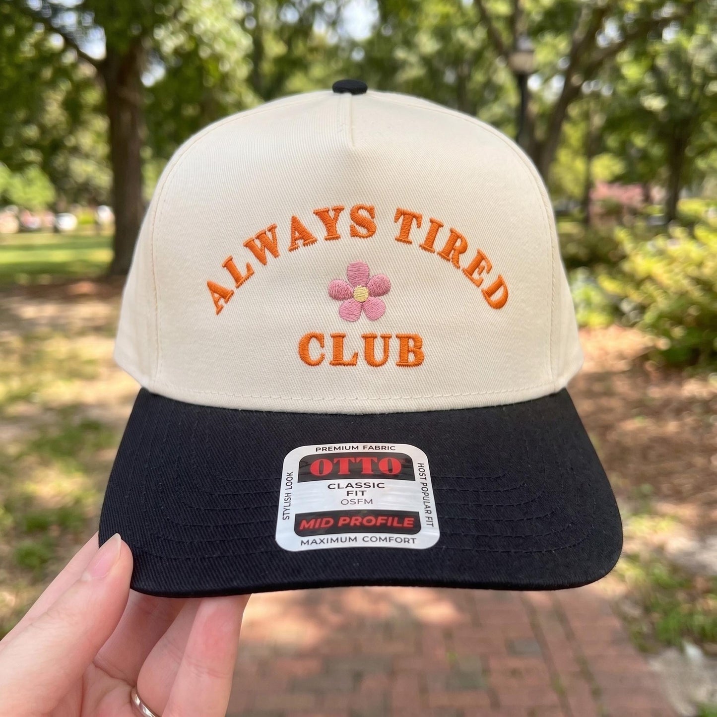 Embroidered 'Always Tired Club' snapback cap with black brim and playful floral detail