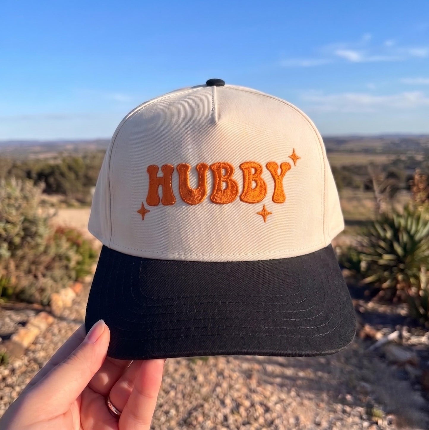 Hubby' embroidered baseball cap in cream and black with orange text, outdoors