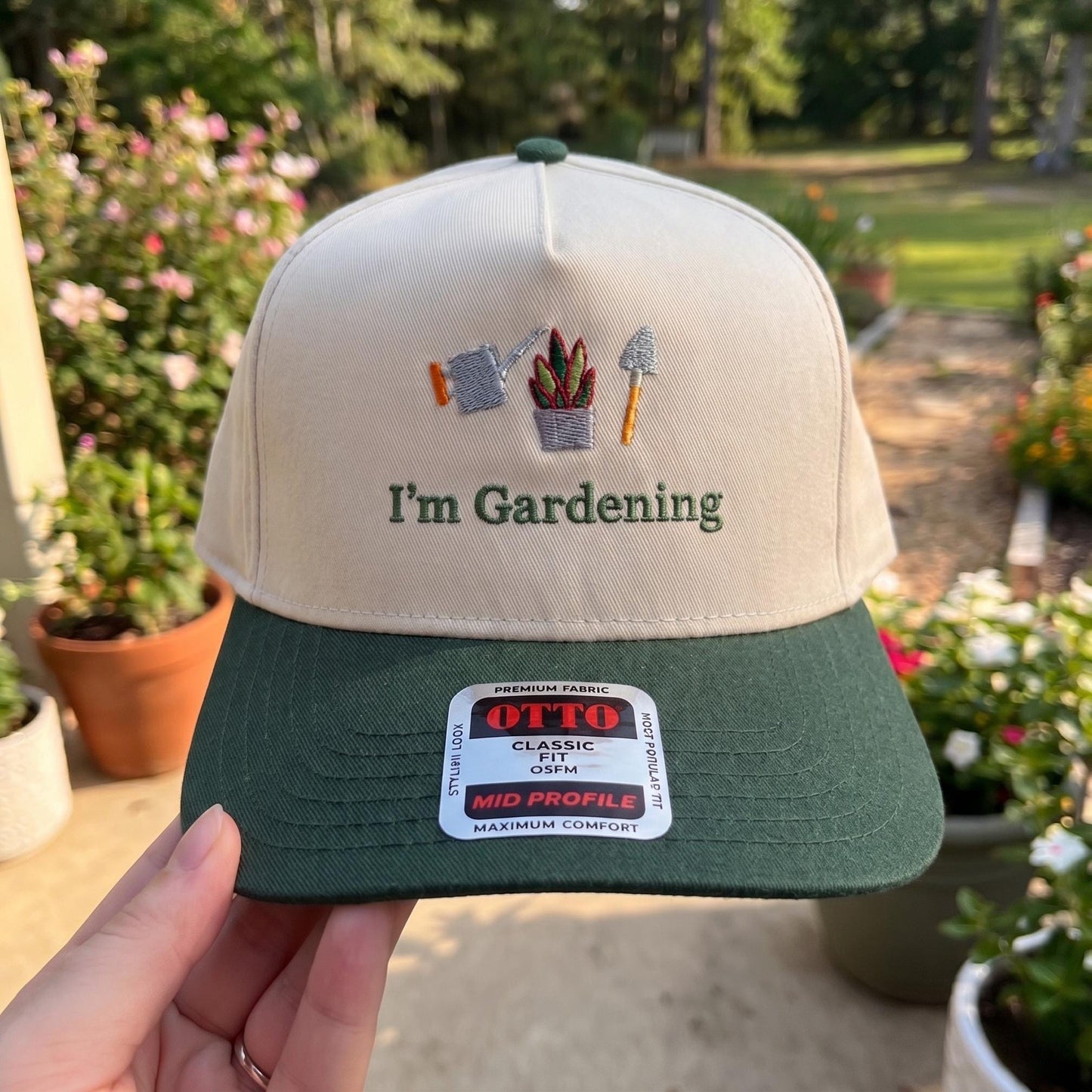 Gardening hat with embroidered watering can, plant, and trowel in beige and green setting