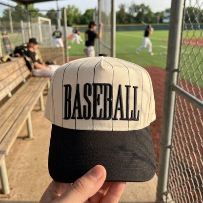 Close-up of a pinstripe baseball hat with dark brim and embroidered BASEBALL text at a baseball field