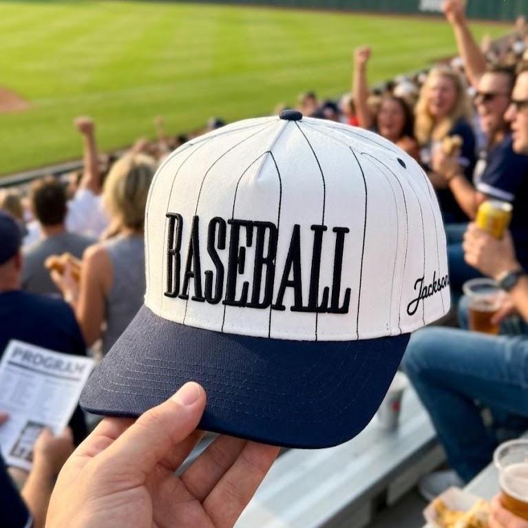 White baseball pinstripe hat with bold black embroidered BASEBALL lettering and navy brim