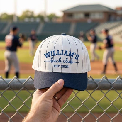 Front view of William’s Beach Club embroidered pinstripe hat held near a baseball field