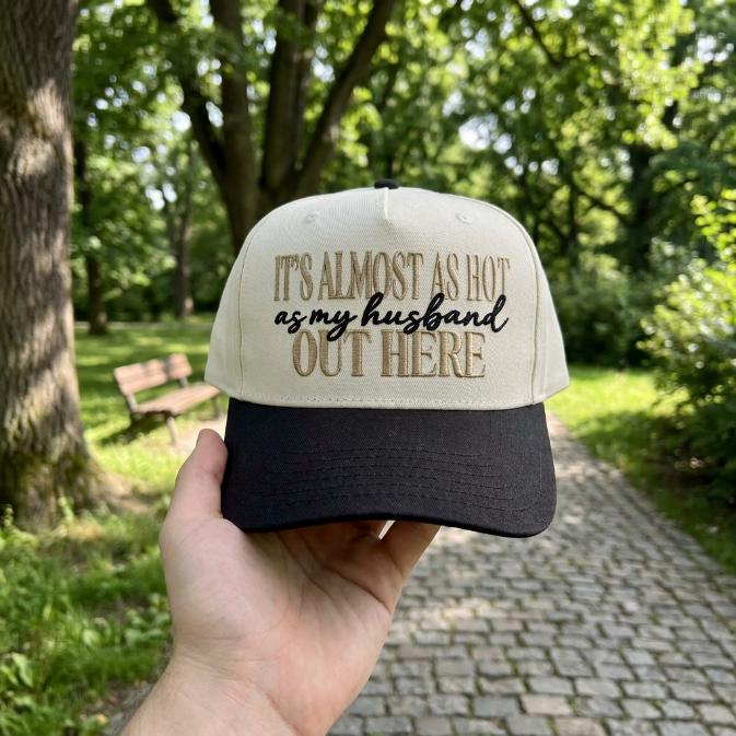 Two-tone embroidered trucker hat with the phrase It's almost as hot as my husband out here