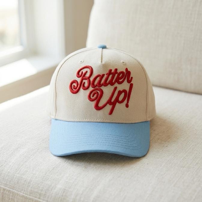 Front view of a cream and light blue Batter Up baseball trucker cap with red script embroidery