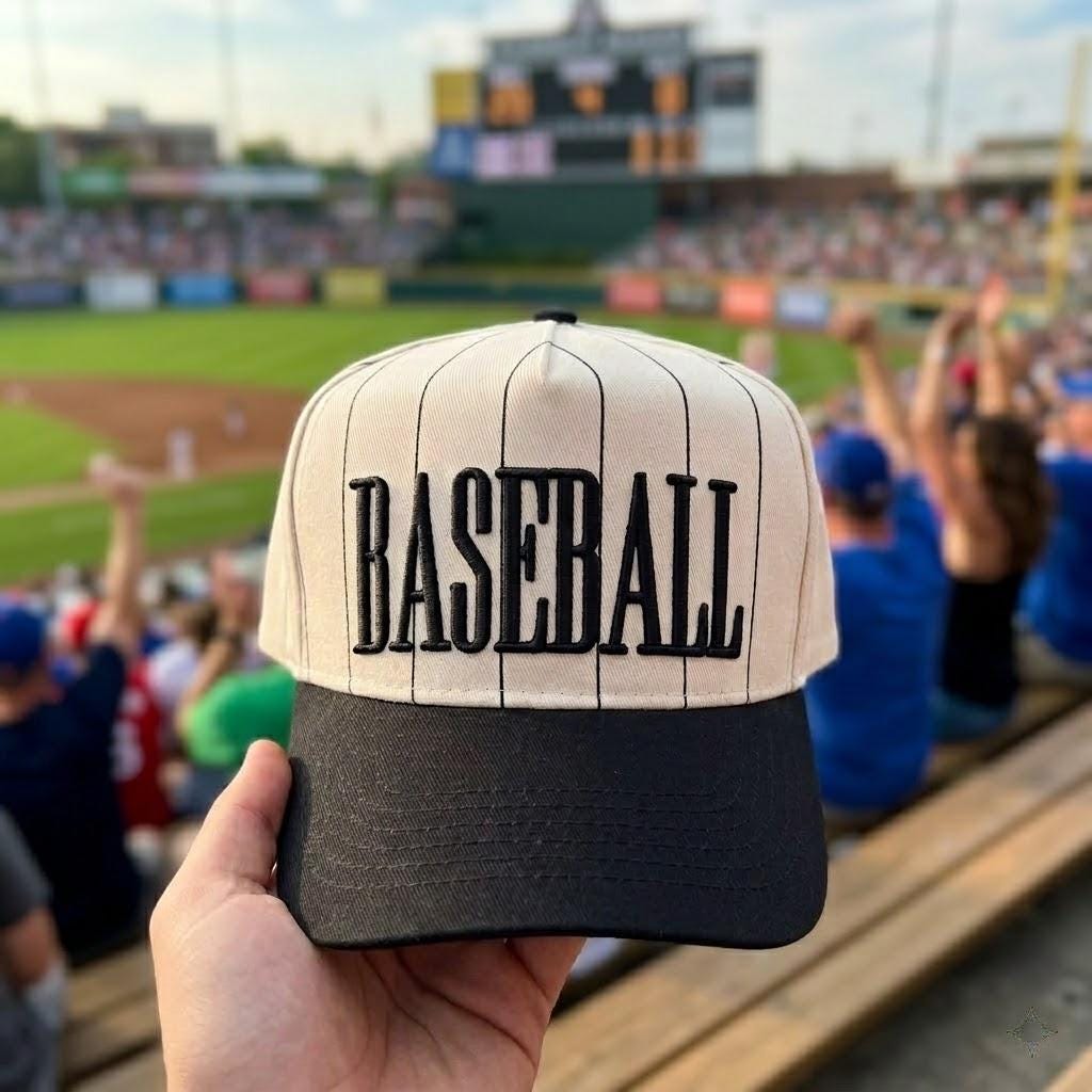 Pinstripe baseball hat with black brim and bold embroidered BASEBALL lettering at a ballpark