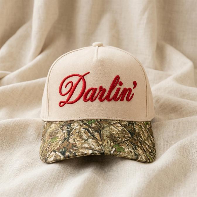 Front view of a neutral Darlin' embroidered hat with red script lettering and camouflage brim