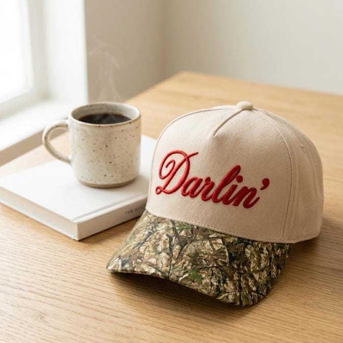 Side view of the Darlin' embroidered hat resting on a wooden table beside coffee