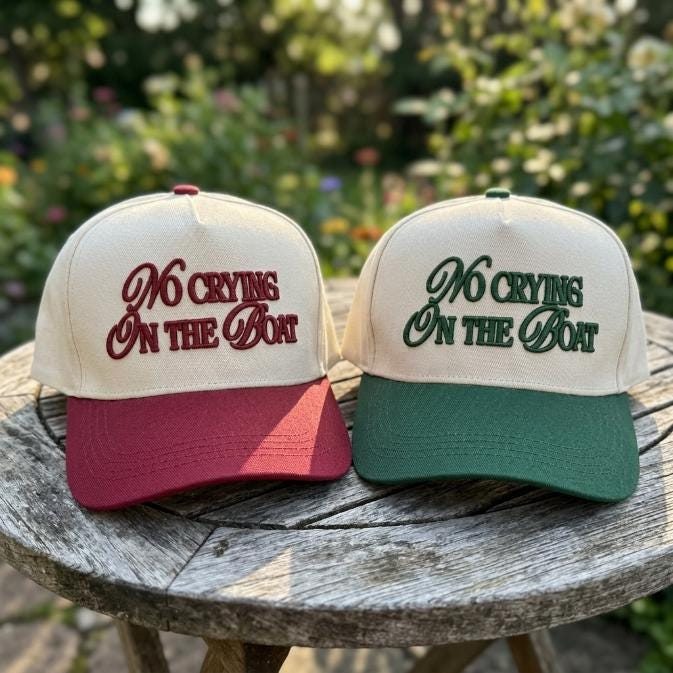 Burgundy and forest green No Crying on the Boat embroidered trucker hats displayed outdoors