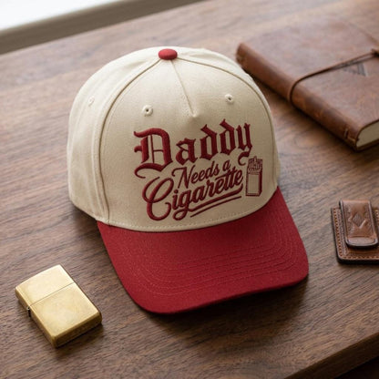 Front view of embroidered Daddy Needs a Cigarette trucker cap on a wooden table
