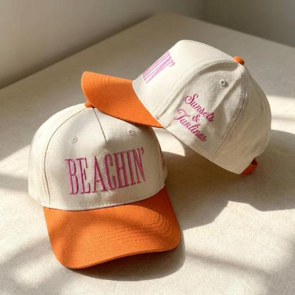 Cream and orange two-tone trucker cap with pink BEACHIN’ embroidery and Sunsets & Tanlines side lettering