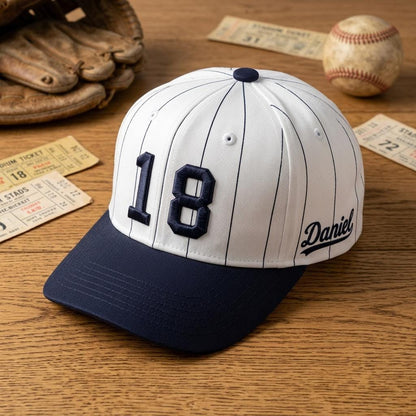 White pinstripe baseball hat with navy brim, number 18, and Daniel lettering displayed with baseball memorabilia