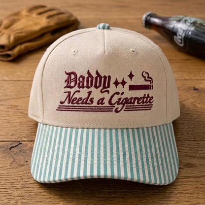 Retro embroidered Daddy Needs a Cigarette hat on a wooden table