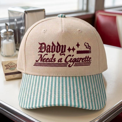 Khaki embroidered hat with Daddy Needs a Cigarette lettering and light blue striped bill