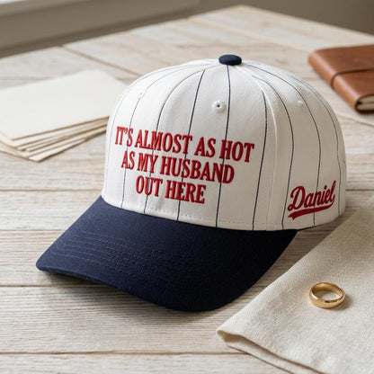 White and navy pinstripe hat with red text reading It’s Almost as Hot as My Husband Out Here