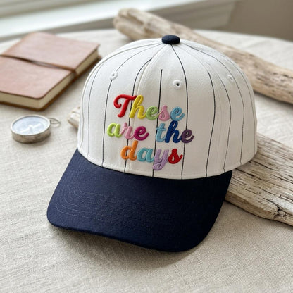 White pinstripe hat with multicolor “These Are the Days” embroidery displayed indoors