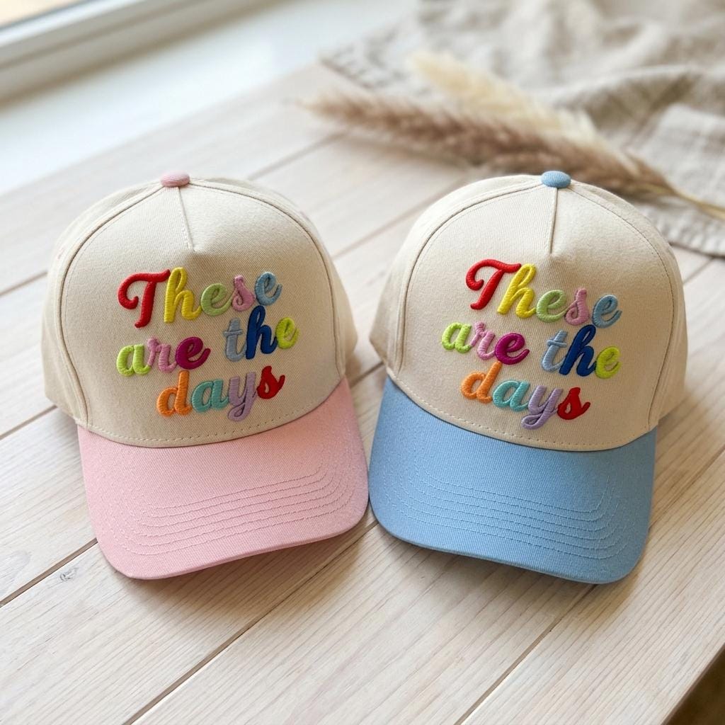 Pink and light blue These are the days embroidered trucker hats displayed on a wood surface