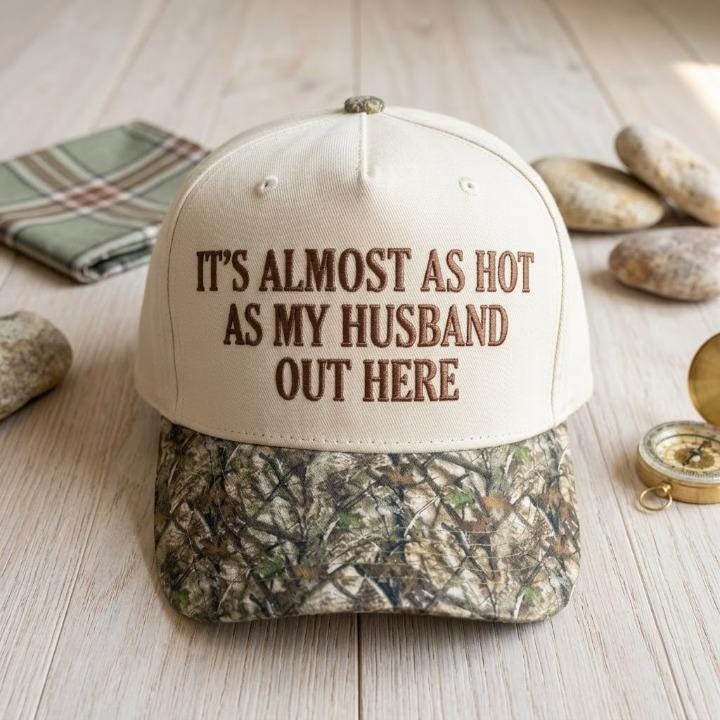 Funny embroidered camo hat displayed outdoors on a rustic fence