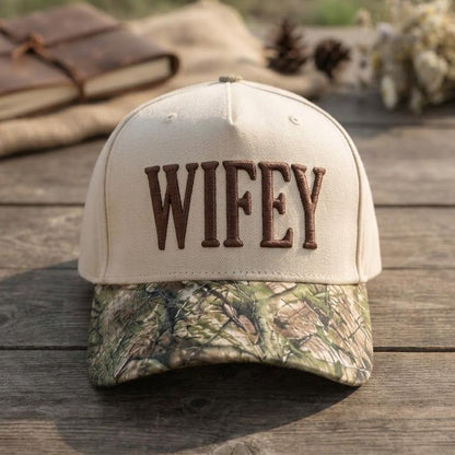 Close-up of cream Wifey trucker hat with raised brown lettering and camo bill