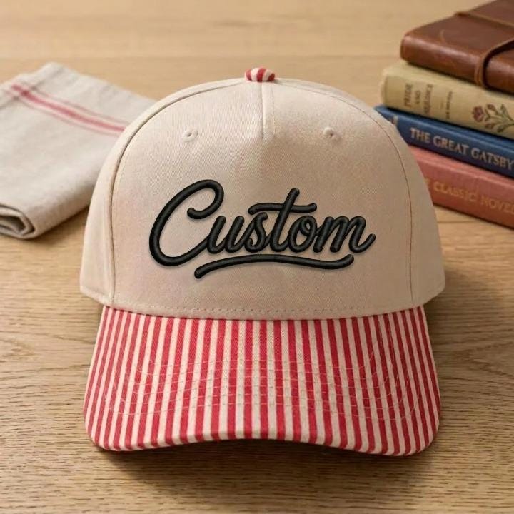 Cream Custom script hat with red striped bill displayed on a wooden table