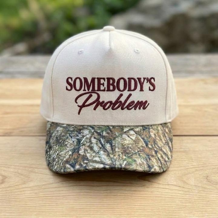 Cream Somebody’s Problem statement hat displayed on a wooden surface