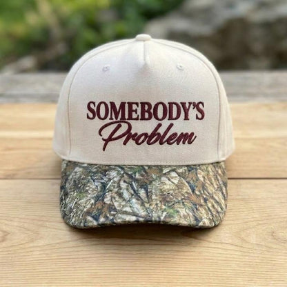 Cream Somebody’s Problem statement hat displayed on a wooden surface