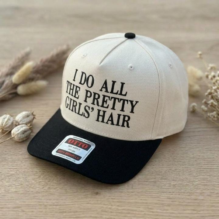 Angled view of cream and black two-tone trucker hat with hair slogan