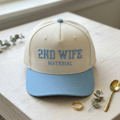 Front view of a cream and light blue 2ND WIFE MATERIAL embroidered trucker hat