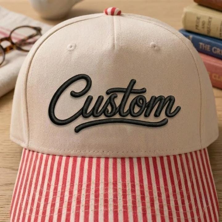 Close-up of black Custom script embroidery on cream hat with red striped bill
