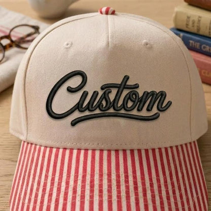 Close-up of black Custom script embroidery on cream hat with red striped bill