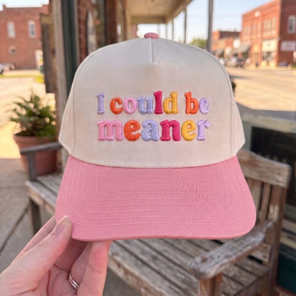 Embroidered cap with colorful 'I Could Be Meaner' text, cream crown with pink brim, displayed in outdoor setting