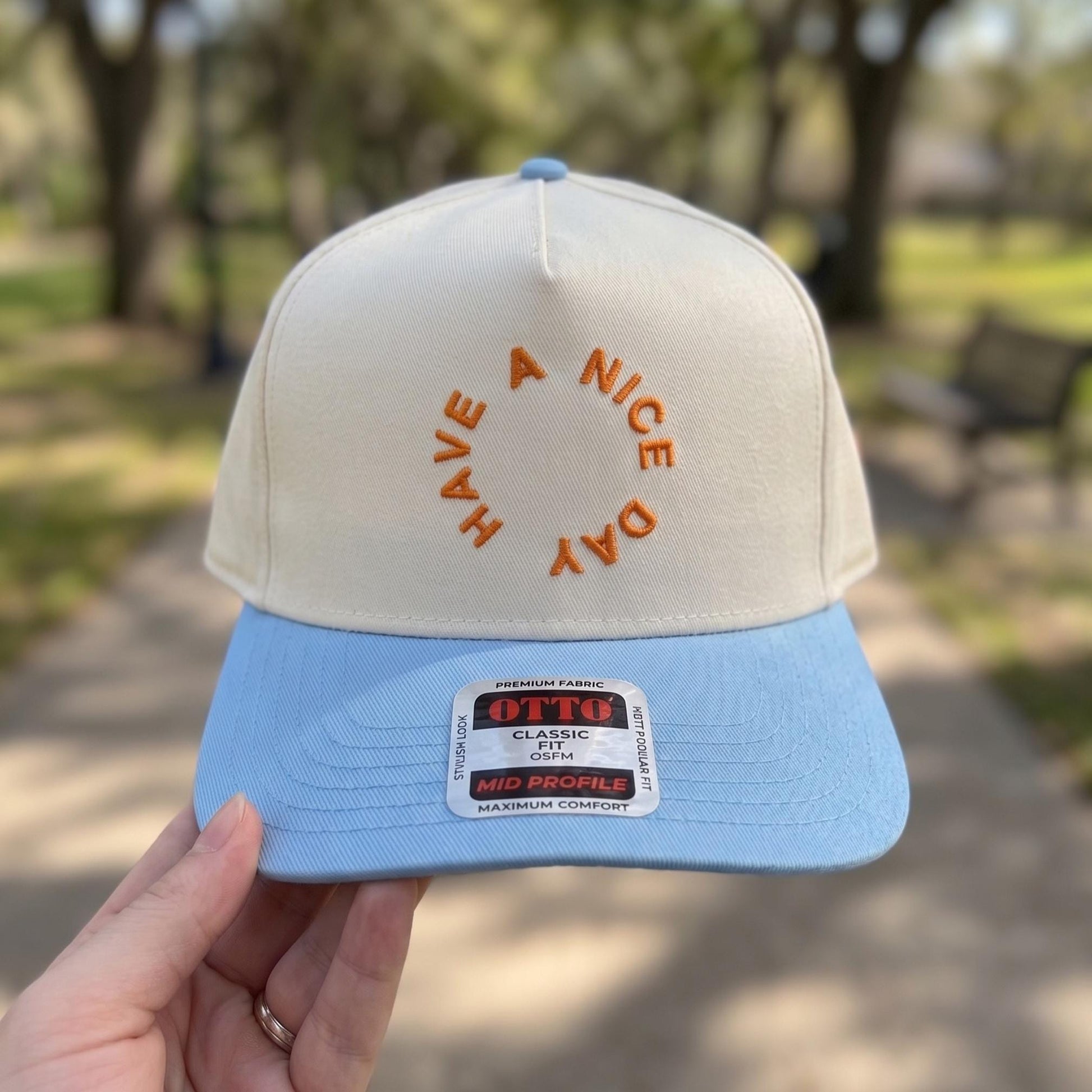 Stylish baseball cap with 'Have a Nice Day' embroidered in orange on a cream and blue two-tone design.