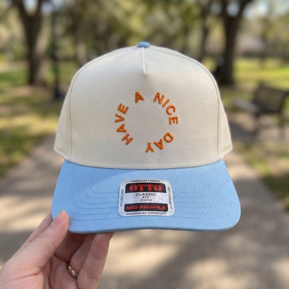 Stylish baseball cap with 'Have a Nice Day' embroidered in orange on a cream and blue two-tone design.