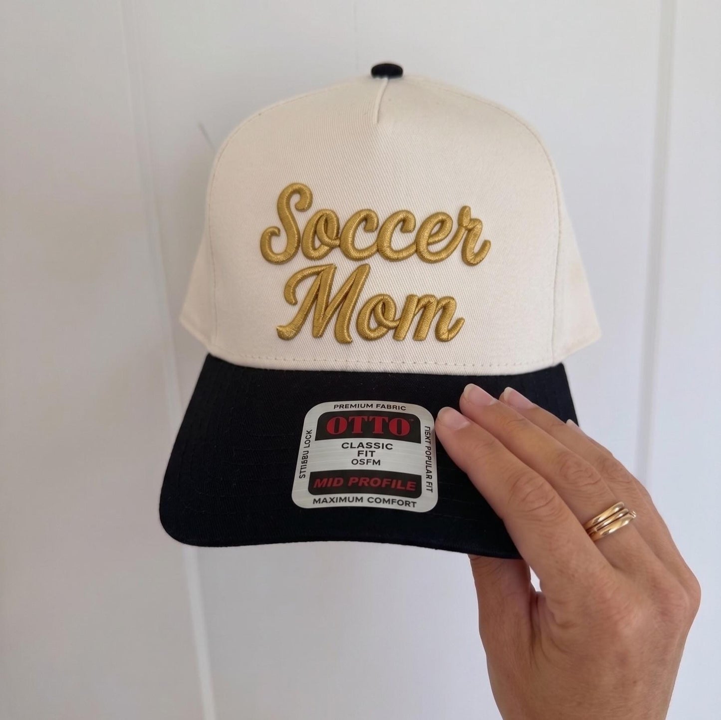 Embroidered 'Soccer Mom' hat with a cream front panel and black brim, stylish trucker cap