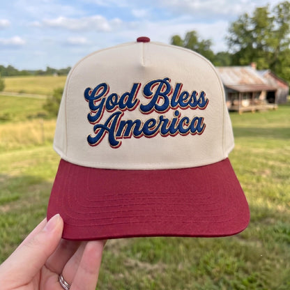Patriotic trucker hat with 'God Bless America' embroidery in red and beige on a grassy field