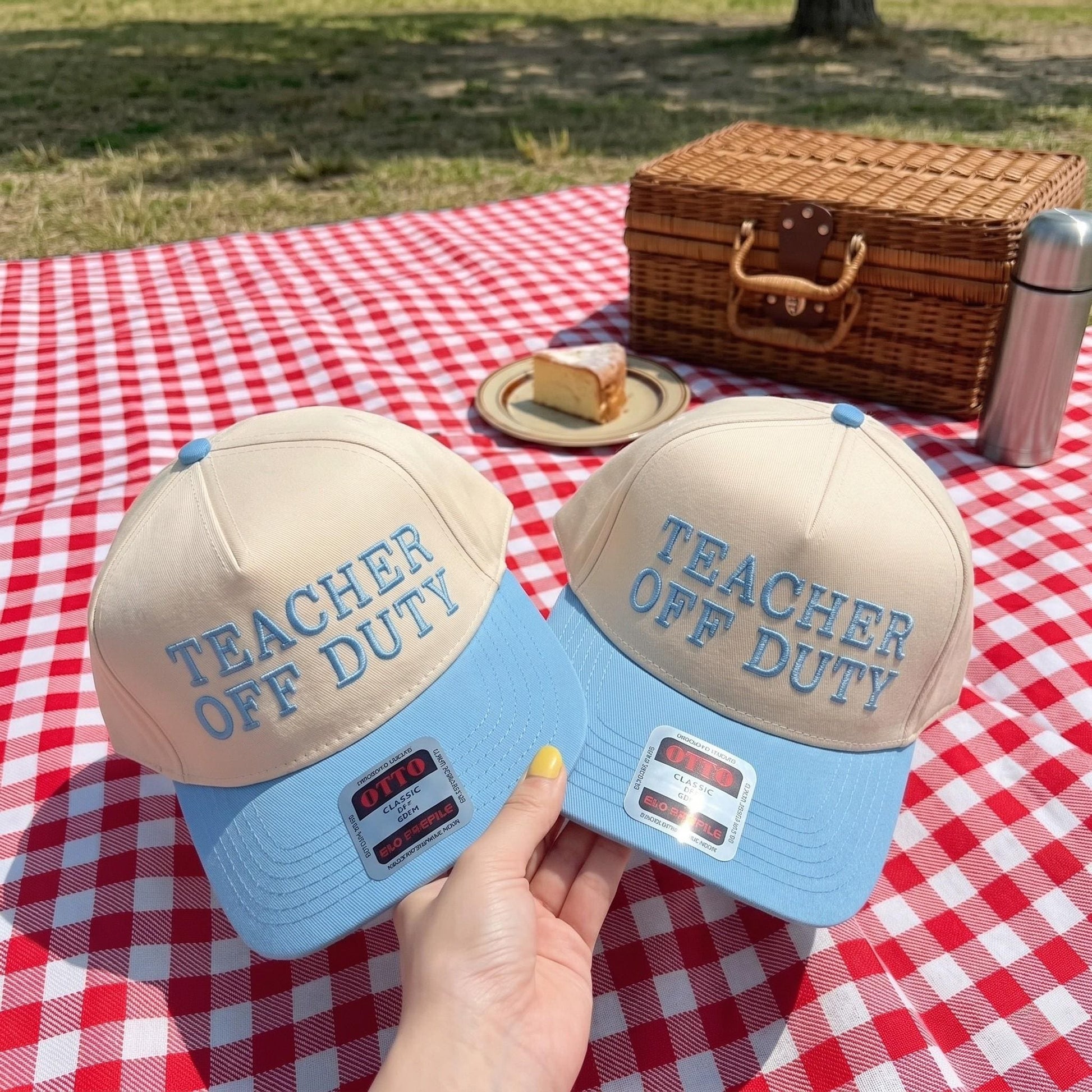 Teacher Off Duty baseball cap with cream crown and blue brim on picnic blanket
