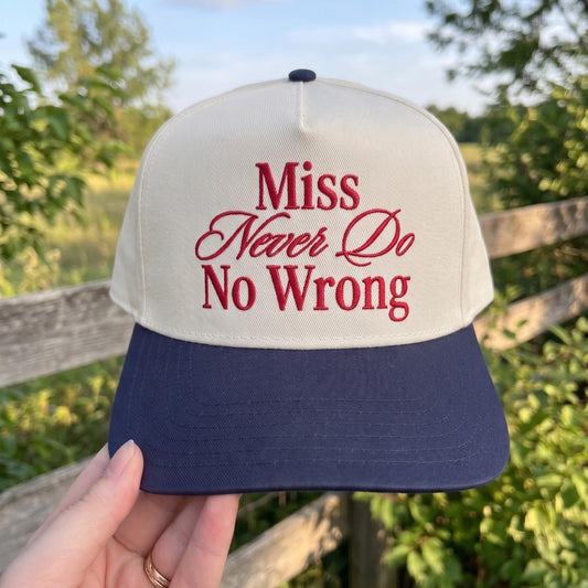 Trendy two-tone cap with 'Miss Never Do No Wrong' embroidery in red on a cream background and navy brim, outdoor setting