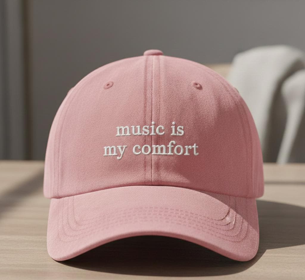 Pink baseball cap with 'music is my comfort' embroidered text, casual style, displayed on a wooden table