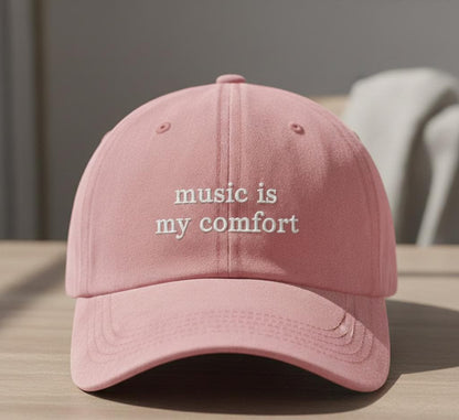 Pink baseball cap with 'music is my comfort' embroidered text, casual style, displayed on a wooden table