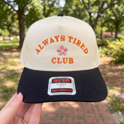Embroidered 'Always Tired Club' snapback cap with black brim and playful floral detail