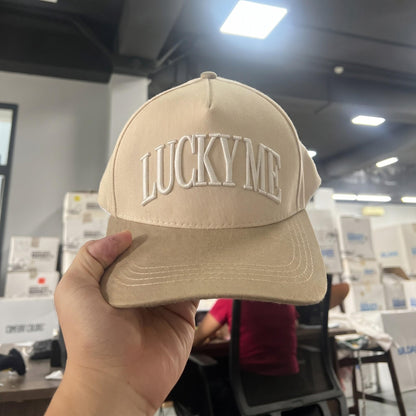 Beige 'Lucky Me' baseball cap with embroidered text displayed indoors