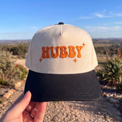 Hubby' embroidered baseball cap in cream and black with orange text, outdoors