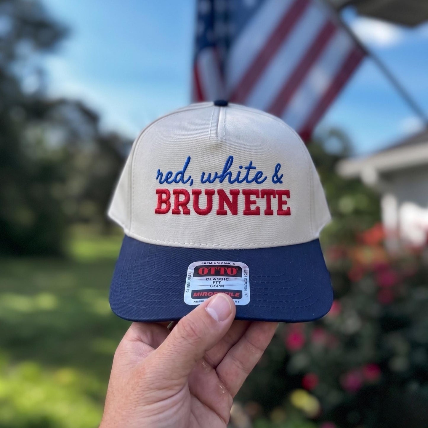 Patriotic trucker hat with 'red, white & brunette' embroidery in a garden setting