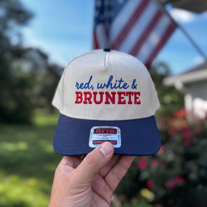 Patriotic trucker hat with 'red, white & brunette' embroidery in a garden setting