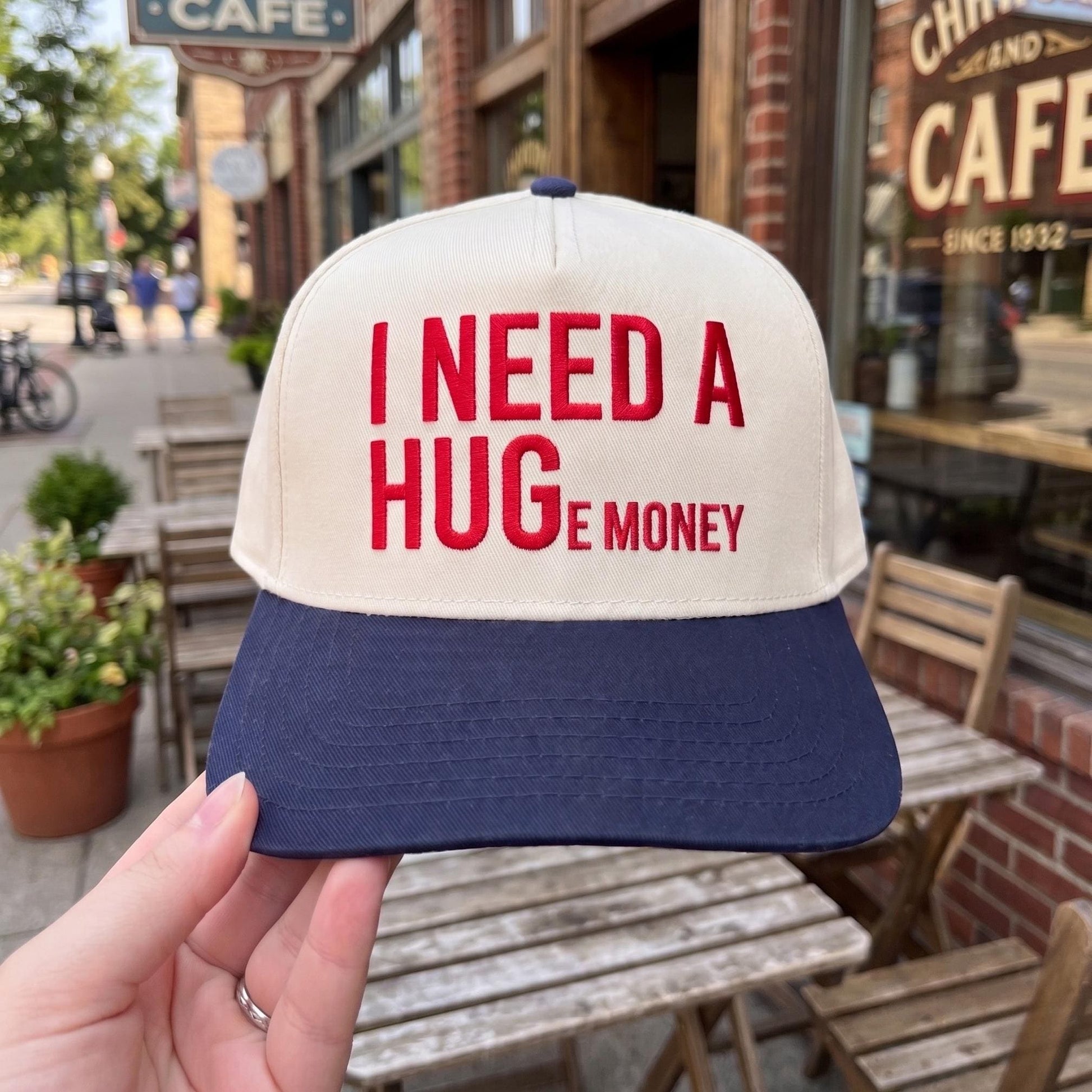 Novelty baseball cap with 'I Need A Huge Money' quote in red embroidery, white crown, navy brim