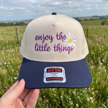 Inspirational embroidered cap with beige crown and navy blue brim featuring 'enjoy the little things' and daisy design
